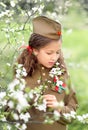 Portrait of a girl in military uniform on Victory Day on May 9 in a blooming garden. A child on the background of a cherry blossom