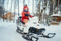 portrait of a girl in a red hat and scarf sits on a snowmobile in a snowy forest on a cold day Royalty Free Stock Photo