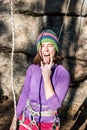 Portrait of girl rock climber shows tongue happy and cheerful, standing at rock inharness with rope and quickdraws