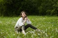 Portrait of a girl sitting in a field on the spring grass among dandelion flowers. Cheerful girl enjoys Sunny spring weather. Royalty Free Stock Photo