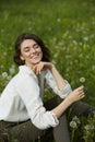 Portrait of a girl sitting in a field on the spring grass among dandelion flowers. Cheerful girl enjoys Sunny spring weather. Royalty Free Stock Photo