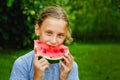 Portrait of a girl with a slice of watermelon in nature on a background of greenery. The child bites off a piece of red watermelon Royalty Free Stock Photo