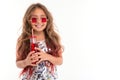 Portrait of girl in glittery dress and stylish square red sunglasses, holding glass bottle with red drink isolated Royalty Free Stock Photo