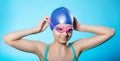 Portrait of a girl sportswoman in a bathing cap and glasses. The girl wears diving goggles. A bright blue background. Royalty Free Stock Photo
