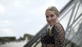 A portrait girl standing near the Louvre glass pyramid on cloudy sky background. Action. Sexy blond plus size model