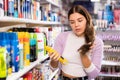 Portrait of girl standing near shelves of hair care products and looking at her hair during choosing hairmousse Royalty Free Stock Photo