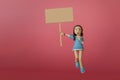 Portrait girl wearing blue oversized shirt, shocked, excited, looking straight, holding a blank sign, jumping on pink background.