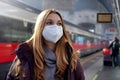 Portrait of girl wearing KN95 FFP2 medical face mask with moving train on background on train station. Copy space