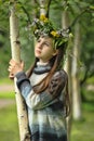 Girl with a wreath of wild flowers on her head near a birch