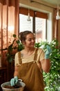 Portrait of glad female gardener smiling, holding green seedling while transplanting plant in pot with dirt or soil