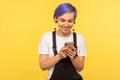 Portrait of glad hipster girl using cell phone, texting or reading message with good news. yellow background, indoor studio shot