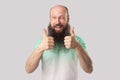 Portrait of glad satisfied middle aged bald man with long beard in green t-shirt standing, thumbs up, winking and toothy smile and Royalty Free Stock Photo