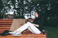 Portrait of a glamorous young woman holding on her knees a book while sitting on a wooden bench. Soft colours, awesome place