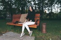 Portrait of a glamorous young woman holding on her knees a book while sitting on a wooden bench. Soft colours, awesome place