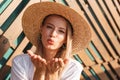 Portrait of glamour seductive woman 20s in straw hat and swimwear giving air kiss to you while standing against wooden beams, on Royalty Free Stock Photo