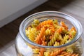 A portrait of a glass pot, jar or bowl full of spirelli in three different colors, orange, yellow and green. The uncooked Royalty Free Stock Photo