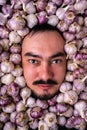 Portrait of a gloomy bearded man in garlic. A man`s head among garlic bulbs