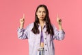 Portrait of gloomy and displeased, young frowning girl in denim jacket, grimacing looking and pointing fingers up