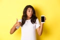 Portrait of good-looking african american female model, recommending an app, showing mobile phone and look excited Royalty Free Stock Photo