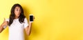 Portrait of good-looking african american female model, recommending an app, showing mobile phone and look excited Royalty Free Stock Photo