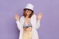 Portrait of good looking pretty young woman wearing panama, white shirt and swimming suit, posing isolated over purple background Royalty Free Stock Photo