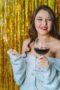 Smiling young woman with long hair, red lips hold indian light and wine glass wearing cardy on golden tinsel background