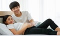 Portrait of a good-looking young Asian man and woman laying on a bed together. They are smiling happily and touching the belly of Royalty Free Stock Photo