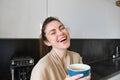 Portrait of good-looking young woman, drinking coffee in the kitchen, enjoying her morning routine and smiling at the Royalty Free Stock Photo