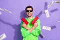 Portrait of good mood cheerful guy brunet hairdo wear green hoodie hold guns shooting money banknotes isolated on violet