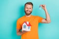 Portrait of good mood optimistic guy with blond hairdo wear orange t-shirt hand hold small house keys isolated on teal Royalty Free Stock Photo