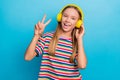 Portrait of good mood positive teen girl wear colorful t-shirt in headphones showing v-sign symbol isolated on blue Royalty Free Stock Photo