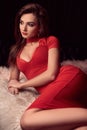 Gorgeous beauty young brunette woman in red dress on a white fur Royalty Free Stock Photo