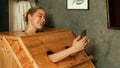 Gorgeous woman playing her mobile phone while using sauna cabinet.Tranquility Royalty Free Stock Photo