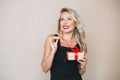 Portrait of gorgeous happy blonde young woman with bright makeup in evening dress with gift box in hands on beige background Royalty Free Stock Photo