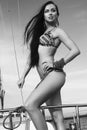 Portrait of a gorgeous long-haired brunette in stylish swimsuit with awesome tan standing on the aft of a sailing yacht. Sunny