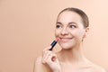 Portrait of gorgeous smiling woman holding rosy lipstick in hand. Model posing in studio and looking Royalty Free Stock Photo