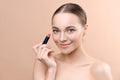 Portrait gorgeous smiling woman holding rosy lipstick in hand. Model posing in studio and looking in Royalty Free Stock Photo