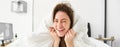 Portrait of gorgeous smiling woman, lying in bed covered in duvet, has messy hair, looking happy, relaxing in her Royalty Free Stock Photo