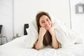 Portrait of gorgeous smiling woman, lying in bed covered in duvet, has messy hair, looking happy, relaxing in her Royalty Free Stock Photo