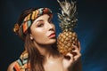 Portrait of Gorgeous woman with colourful bandana on head, holding pineapple.