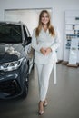 Portrait of gorgeous woman in showroom. Beautiful salesperson standing by car. Blond hair female after buying car