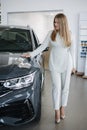 Portrait of gorgeous woman in showroom. Beautiful salesperson standing by car. Blond hair female after buying car