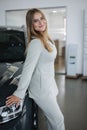 Portrait of gorgeous woman in showroom. Beautiful salesperson standing by car. Blond hair female after buying car