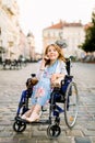 Portrait of a gorgeous young blond woman in a wheelchair enjoying her day and talking on the phone while walking in the Royalty Free Stock Photo