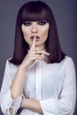 Portrait of gorgeous young dark-haired woman with provocative make up and expressive eyes looking straight with hush gesture