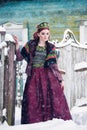 Portrait of a gorgeous young woman wearing russian style dress on a strong frost in a winter snowy day near the fence.