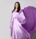 Portrait of graceful brunette woman in lilac evening maxi dress silk gown stands with the hem fluttering in the wind Royalty Free Stock Photo