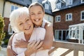 Portrait Of Granddaughter Hugging Grandmother On Bench During Visit To Retirement Home