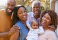 Portrait Of Grandparents With Adult Parents And Baby Granddaughter In Garden At Home Together