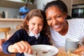 Portrait Of Grandparents In Kitchen With Granddaughter Eating Breakfast Before Going To School